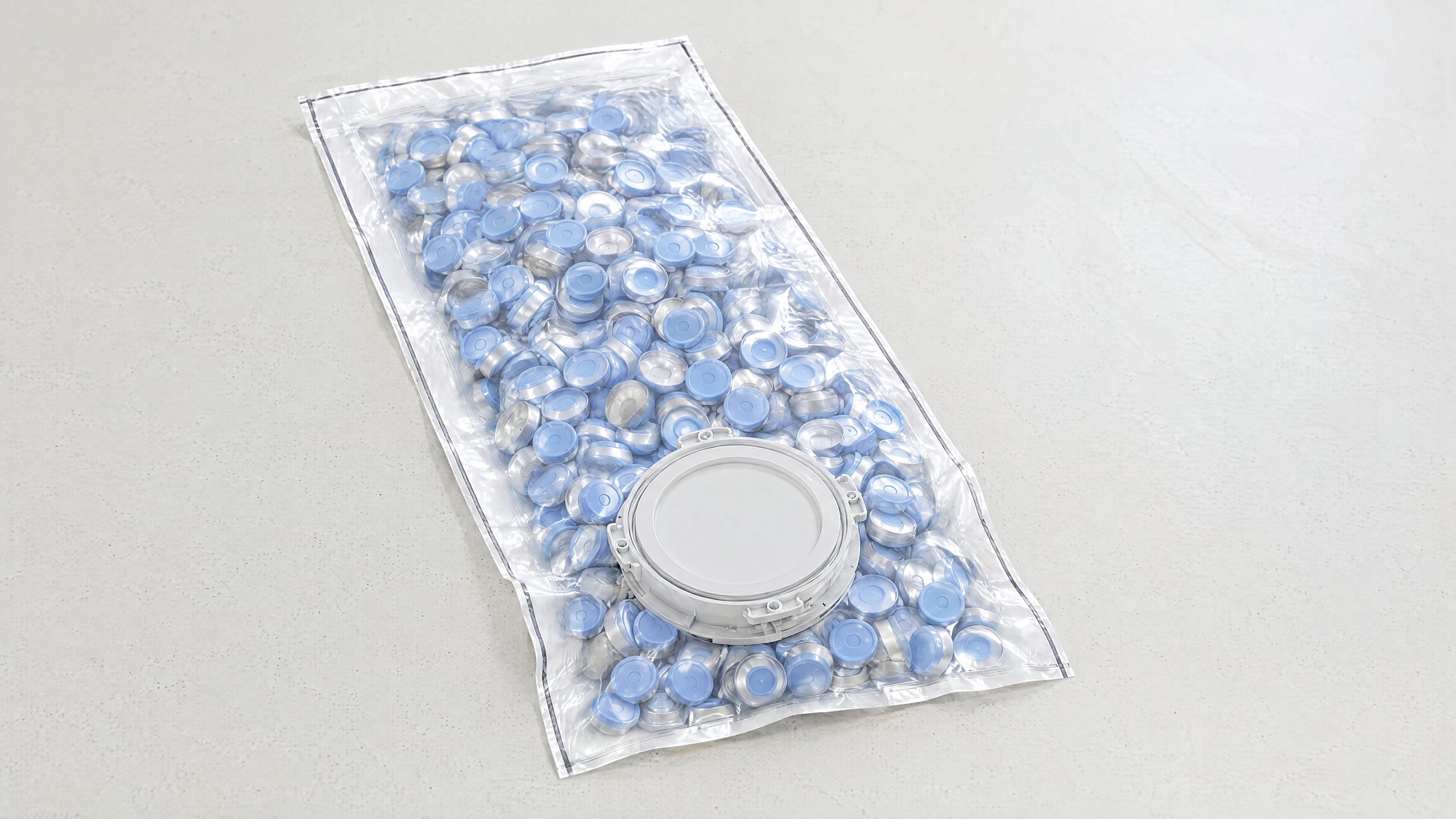 A Pre-loaded DELTAQUANT single-use beta bag filled with aluminium seals and flip-off caps, lying flat on a white table: a flat pouch with the 190 mm beta flange sandwiched into its face, the flange cover facing up.
